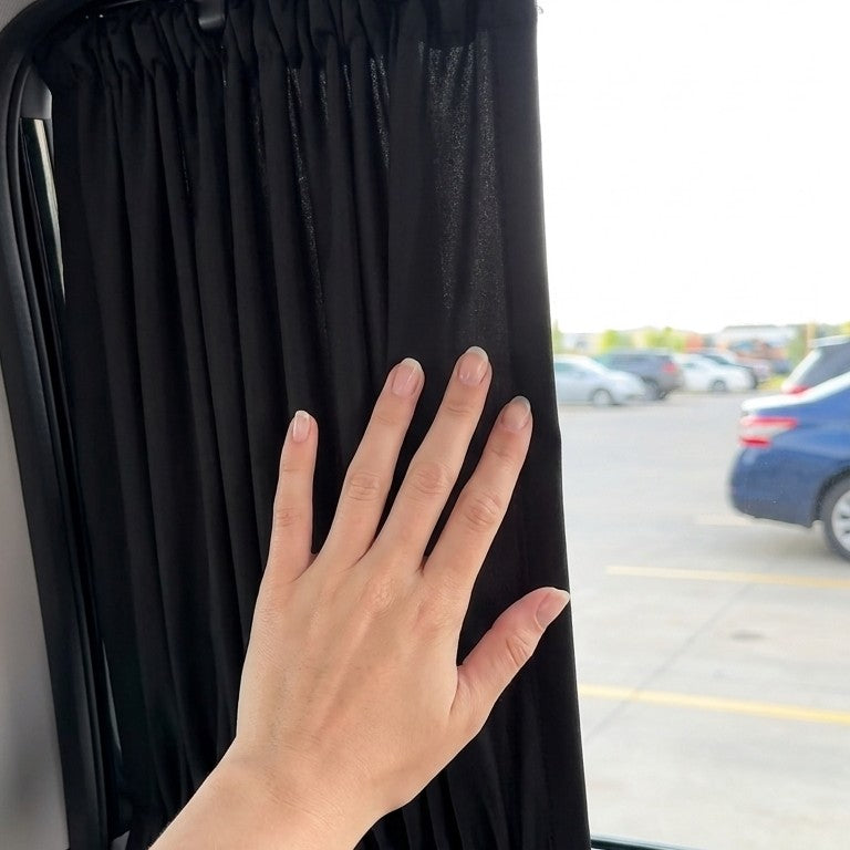A hand sliding a black privacy curtain shut along its rail over a car window